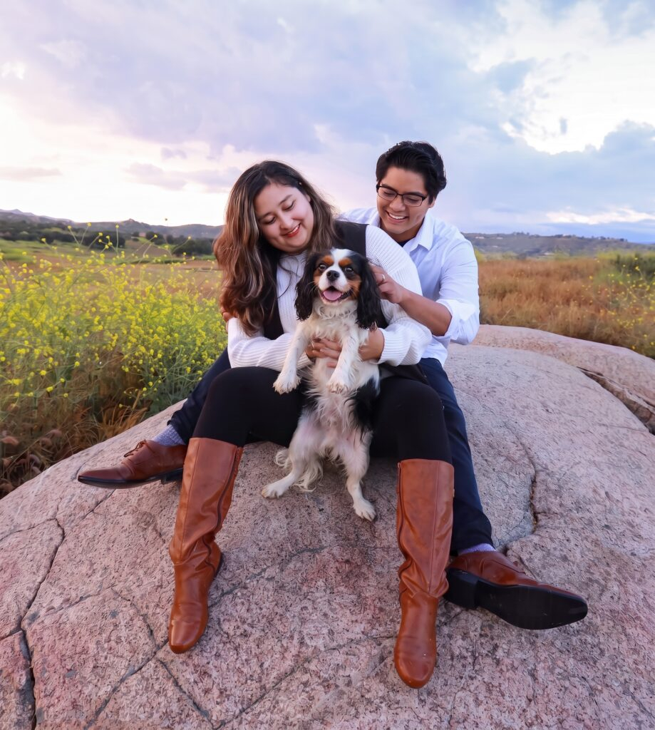 Natalie and David, owners of Lares Petsitting in San Diego, sitting outdoors with their Cavalier King Charles Spaniel